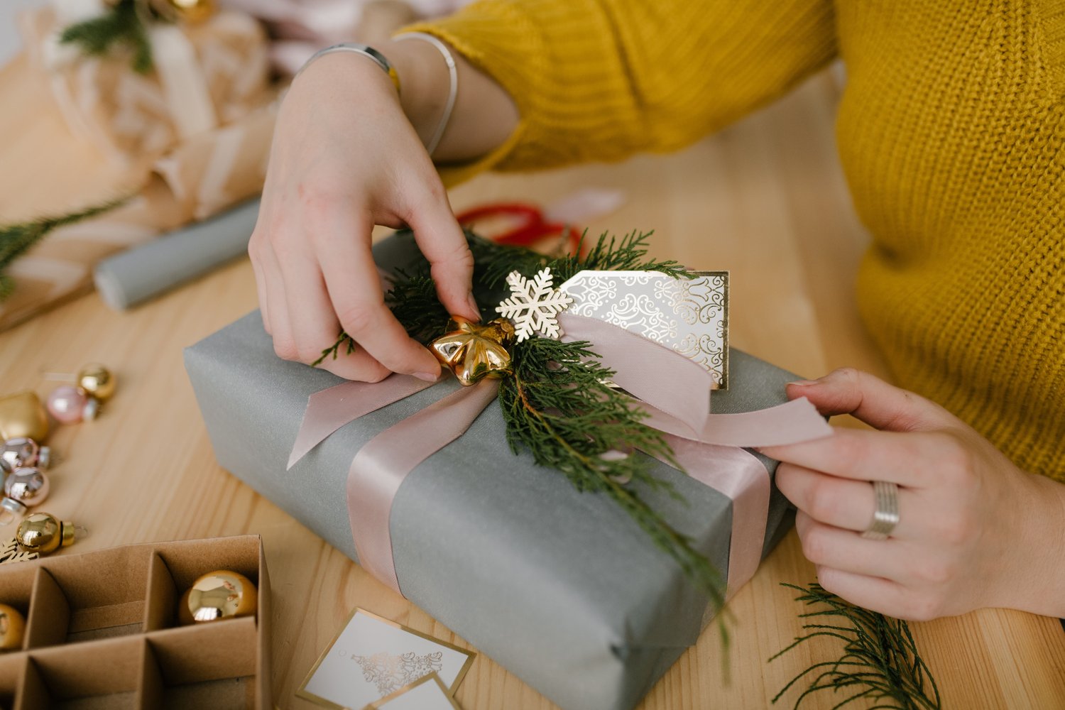 "Hands tying gold ribbon on a luxury Nifty Package Co gift box with a handwritten card."