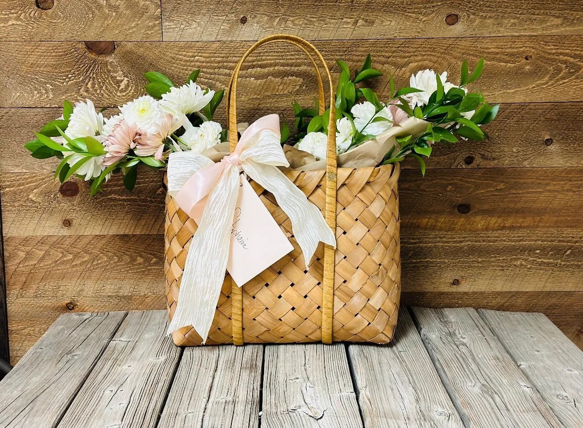French Market Floral Tote featuring white gerbera daisies, blush accents, and Italian Ruscus greenery in a woven market tote with silk ribbon by Nifty Package Co.
