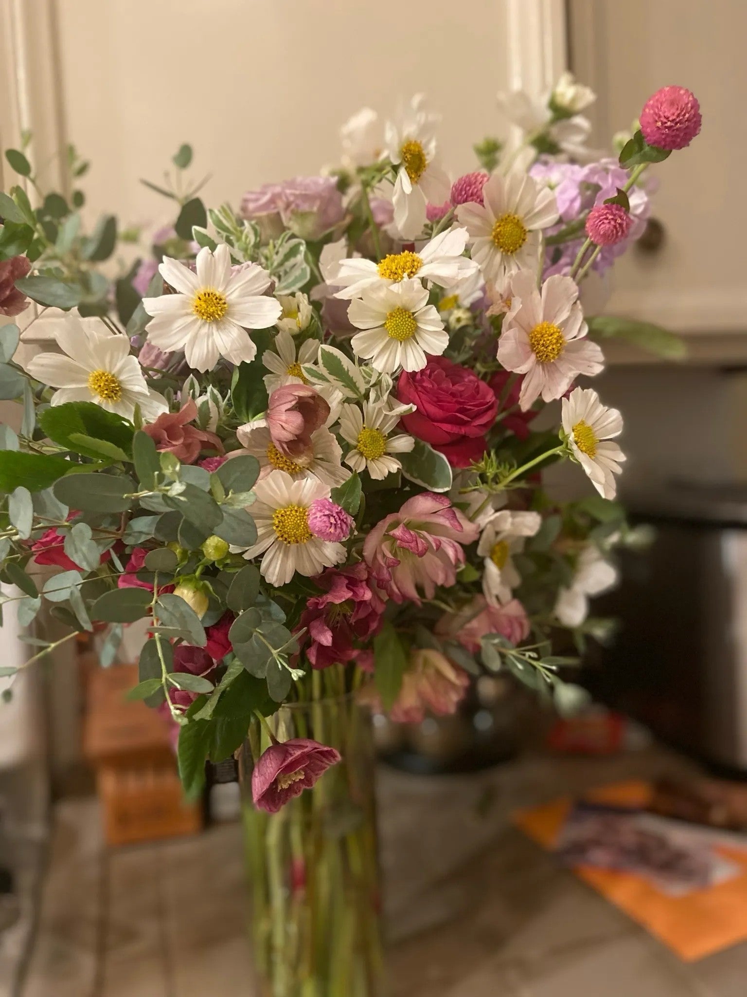 Garden Celebration luxury floral arrangement with white cosmos, deep berry roses, pink ranunculus, and eucalyptus in a tall glass cylinder by Nifty Package Co